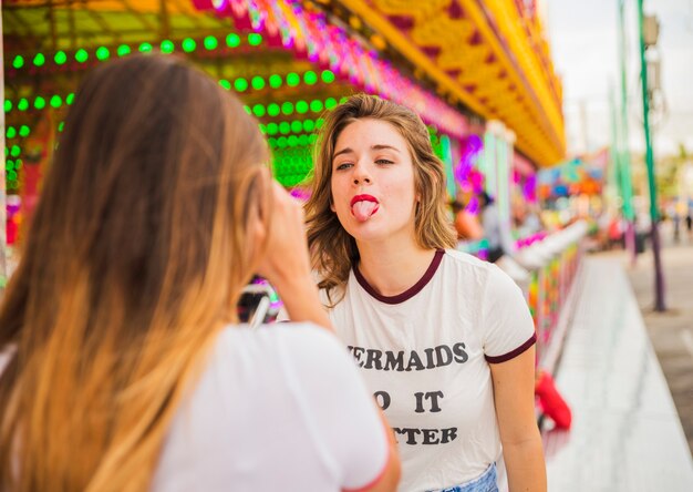 Hintere Ansicht der Frau Foto ihres Freundes machend, der Zunge am Vergnügungspark zeigt