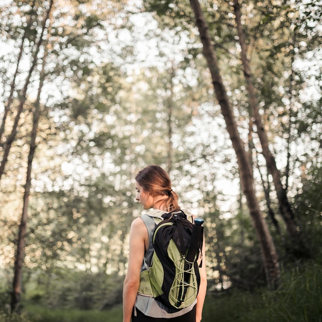 Hintere Ansicht der Frau mit ihrem Rucksack, der im Wald steht