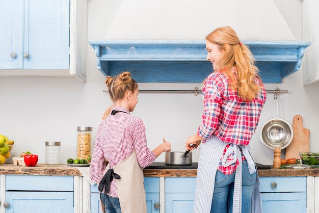 Kostenloses Foto hintere ansicht der mutter und ihrer tochter, die lebensmittel in der küche kochen