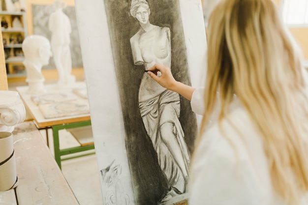Hintere Ansicht der skizzierenden Skulptur des blonden weiblichen Künstlers auf Segeltuch