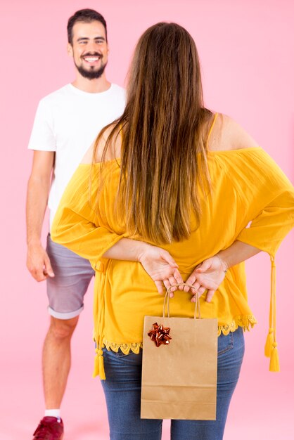 Hintere Ansicht der versteckenden Einkaufspapiertüte der Frau mit rotem Bogen von ihrem Freund
