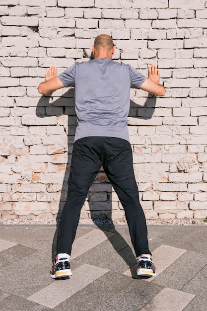 Kostenloses Foto hintere ansicht des athletenmannes lehnend auf backsteinmauer beim handeln von übung