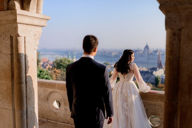 Hintere Ansicht des Hochzeitspaares am sonnigen Tag auf der Spitze eines steinernen Architekturgebäudes mit schöner Stadtlandschaft