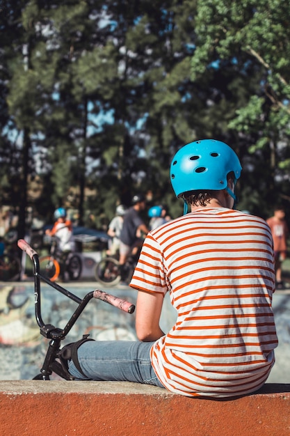 Kostenloses Foto hintere ansicht des jungen blauen sturzhelm mit dem fahrrad tragend, das draußen sitzt