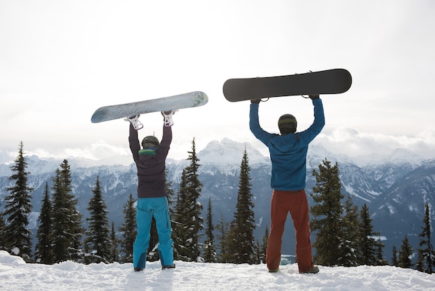 Hintere Ansicht des Mannes und der Frau, die Snowboard am Berg während des Winters halten