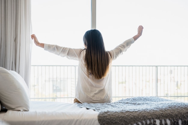 Hintere Ansicht einer Frau, die auf dem Bett ausdehnt ihre Arme sitzt