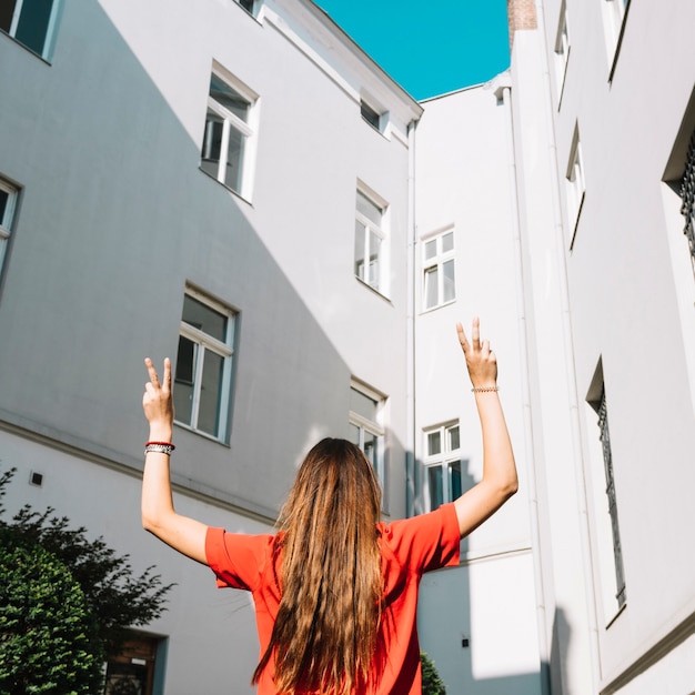 Hintere Ansicht einer Frau, die Friedensgeste nahe Gebäude macht