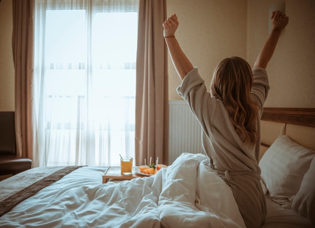 Hintere Ansicht einer Frau, die Körper nach dem Erwachen auf Bett ausdehnt