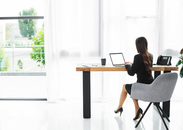Hintere Ansicht einer Geschäftsfrau, die Laptop im modernen Büroinnenraum verwendet