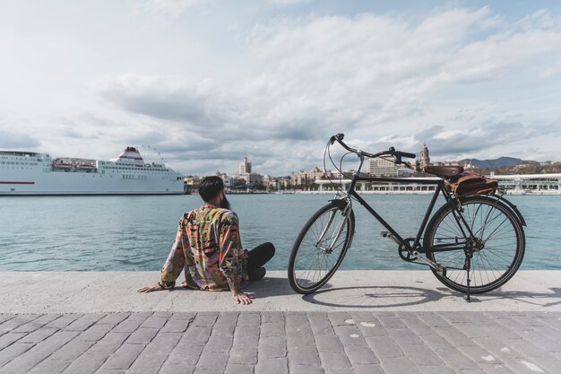 Hintere Ansicht eines Mannes mit dem Fahrrad, das nahe Bucht sitzt