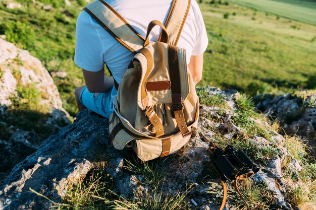 Hintere Ansicht eines Mannes mit dem Rucksack, der auf Felsen sitzt