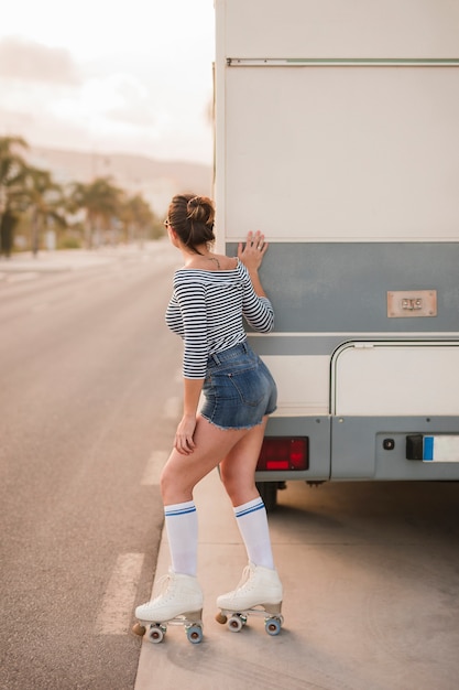 Kostenloses Foto hintere ansicht eines weiblichen schlittschuhläufers, der nahe dem wohnwagen späht auf straße steht
