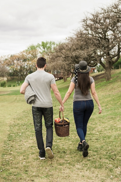 Kostenloses Foto hintere ansicht von den jungen paaren, die mit picknickkorb im park gehen