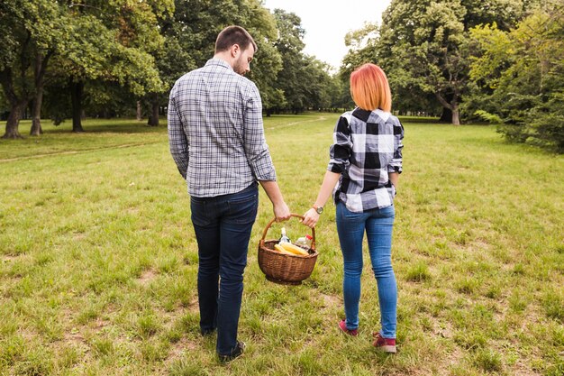 Hintere Ansicht von den Paaren, die Picknickkorb geht im Park halten