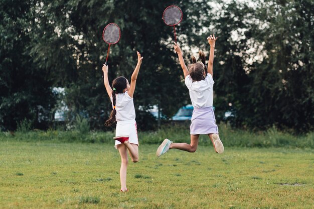 Hintere Ansicht von zwei Mädchen, die in den Park hält Badminton springen