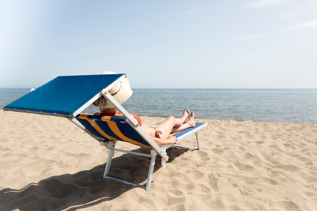 Hintere Ansichtfrau auf dem ein Sonnenbad nehmenden Strandstuhl