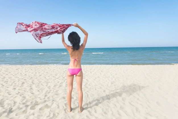 Hintere Ansichtfrau, die auf dem Strand betrachtet das Meer steht