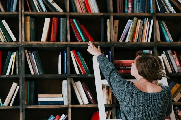 Hintere Ansichtfrau, die Buch vom Regal wählt