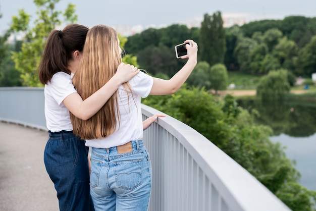 Hintere Ansichtmädchen, die ein selfie auf einer Brücke nehmen