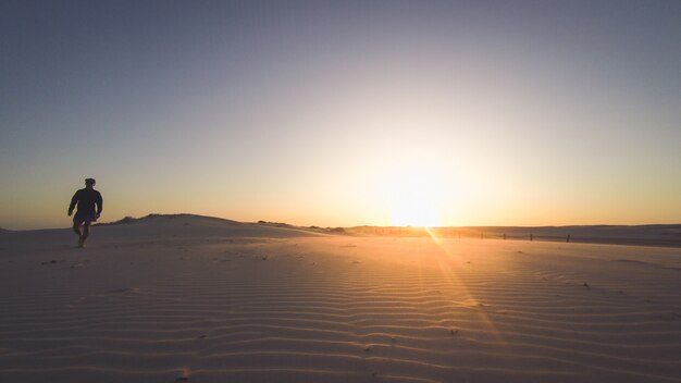 Hintere Ansichtschattenbild eines Läufermannes, der entlang auf den Strand bei Sonnenuntergang mit Sonne im Hintergrund läuft