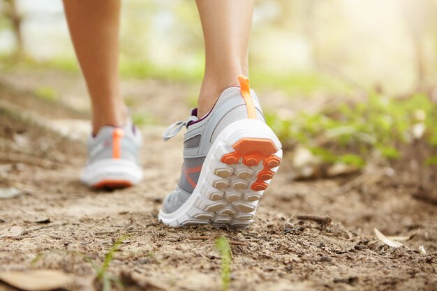 Hinterer abgeschnittener Schuss von athletischen Beinen des Frauenjoggers, der rosa Laufschuhe während der Joggingübung im Freien trägt.