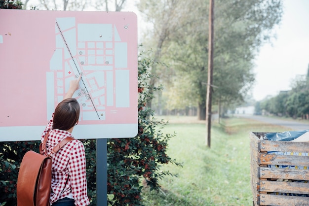 Hinteres Ansichtmädchen mit Rucksack eine Karte im Park überprüfend