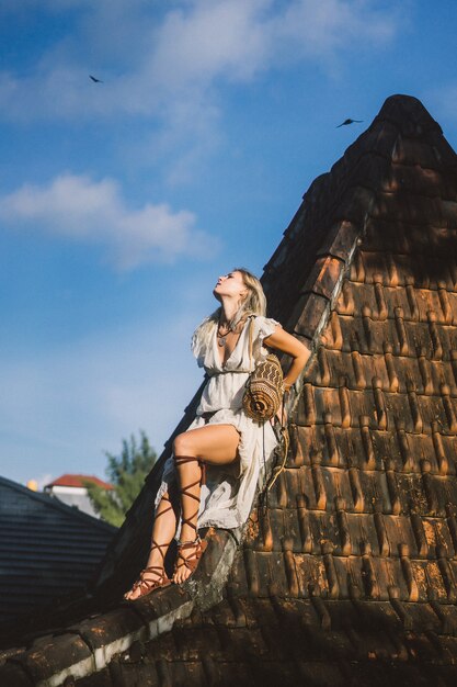 Hippiemädchen mit langen blonden Haaren in einem Kleid auf dem Dach.