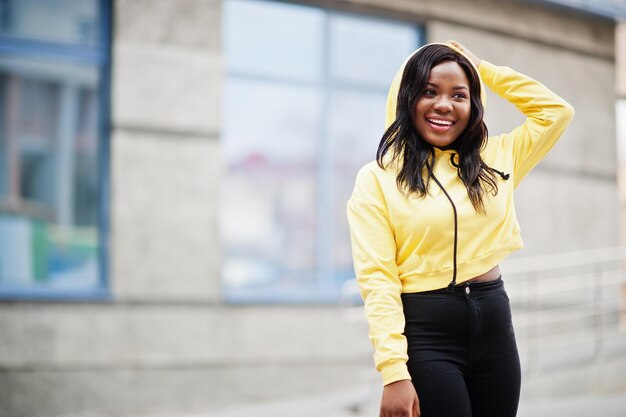 Hipster afroamerikanisches Mädchen mit gelbem Hoodie, das auf der Straße posiert