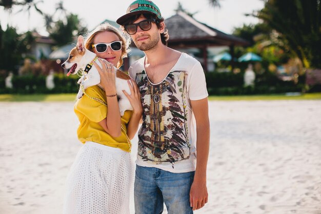 Hipster junges stilvolles hipster-paar in der liebe zu fuß spielen hund welpe jack russell in tropischen strand, weißen sand, cooles outfit, romantische stimmung, spaß haben, sonnig, mann frau zusammen, urlaub