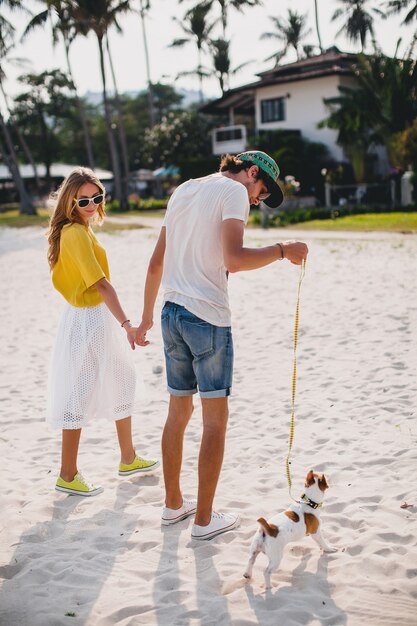 Hipster junges stilvolles Hipsterpaar in der Liebe, die mit Hund im tropischen Strand geht und spielt