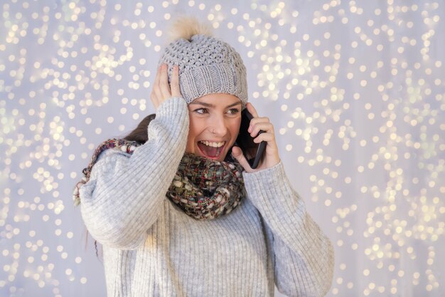 Hispanische Frau, die einen warmen Pullover und einen Hut trägt und sehr aufgeregt am Telefon spricht