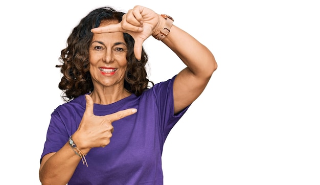 Kostenloses Foto hispanische frau mittleren alters trägt legere kleidung und lächelt, macht mit händen und fingern einen rahmen mit fröhlichem gesicht, kreativität und fotografiekonzept