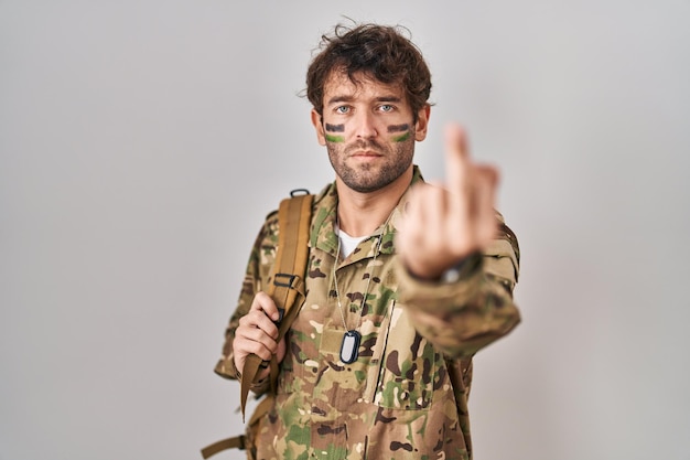 Hispanischer junger Mann in Tarn-Armeeuniform mit unhöflichem und unhöflichem Mittelfinger-Gesichtsausdruck