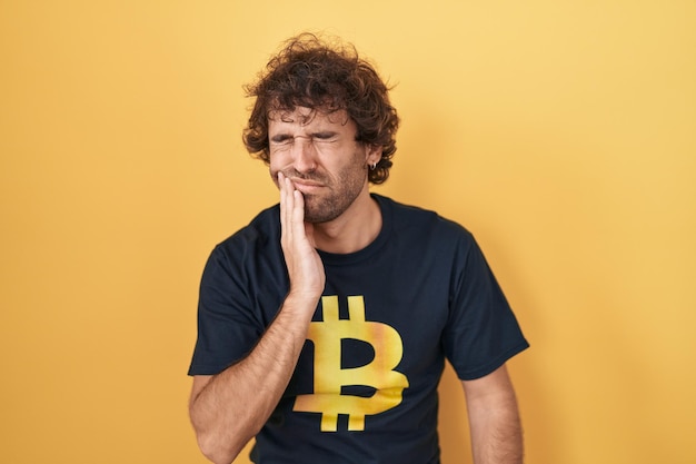 Kostenloses Foto hispanischer junger mann trägt bitcoin-t-shirt und berührt den mund mit der hand mit schmerzhaftem gesichtsausdruck wegen zahnschmerzen oder einer zahnerkrankung an den zähnen. zahnarztkonzept