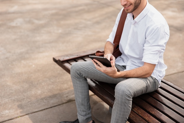 Hochschulstudent, der auf einer Bank sitzt und die Tablette verwendet