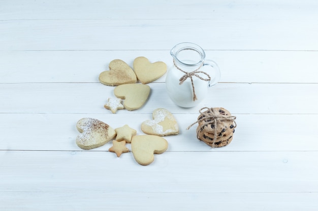 Hochwinkelansicht herzförmig und Sternplätzchen mit Krug Milch auf weißem Holzbretthintergrund. horizontal