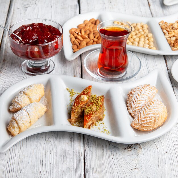 Hochwinkelansicht köstliche Desserts mit Tee, Nüssen, Fruchtmarmelade auf weißem hölzernem Hintergrund.