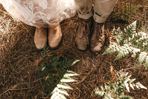 Hochwinkelaufnahme der alten Schuhe der Braut und des Bräutigams, die auf dem trockenen Gras stehen