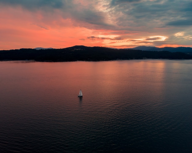 Hochwinkelaufnahme des schönen Meeres mit einem einzelnen Boot, das bei Sonnenuntergang segelt