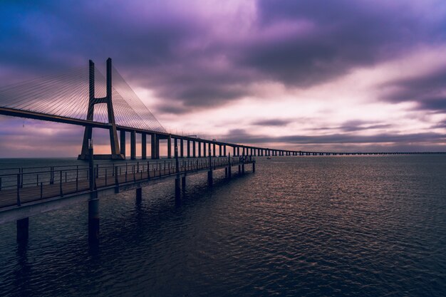 Hochwinkelaufnahme einer Holzbrücke über dem Meer unter dem purpurfarbenen Himmel