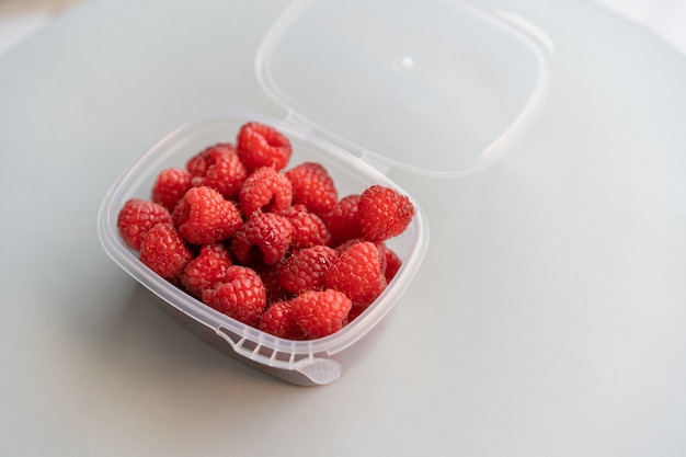 Hochwinkelaufnahme von frischen Himbeeren in einer Plastikbox auf einer weißen Oberfläche