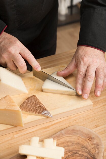 Hochwinkelkoch, der Käse auf Holzbrett schneidet