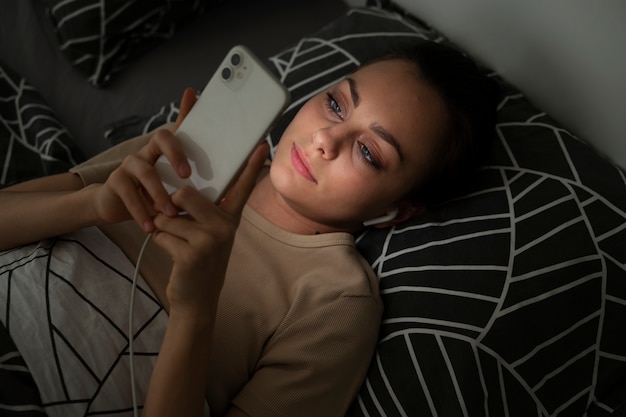 Hochwinkelmädchen, das mit Smartphone im Bett liegt