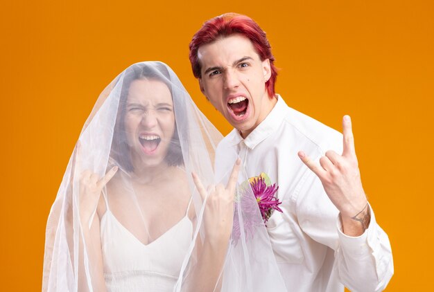 Hochzeitspaar Bräutigam und Braut im Hochzeitskleid posieren zusammen und sehen glücklich und aufgeregt aus und zeigen Rock-Symbol