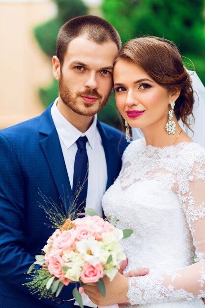 Hochzeitspaar in Liebe küssen und lächeln. Junge hübsche elegante Braut und ihr hübscher Bräutigam, der im grünen Park aufwirft.