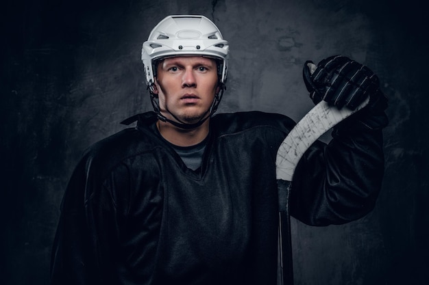 Hockeyspieler in schwarzer Sportbekleidung und weißem Helm hält den Gaming-Stick auf grauem Hintergrund.