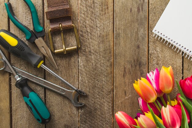 Hölzerne Oberfläche mit Werkzeugen, Blumen und Notizbuch für Vatertag