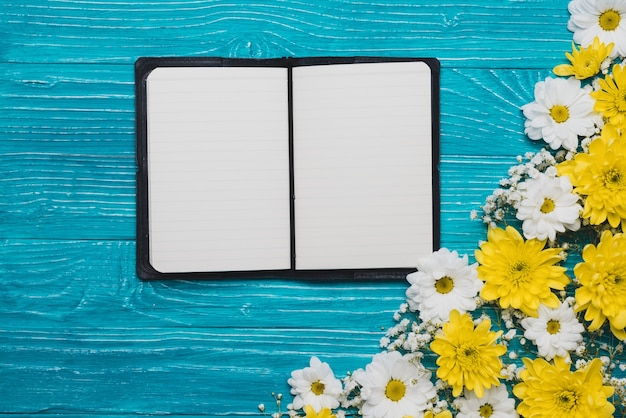 Hölzerner Hintergrund mit offenen Notebook und Blumen