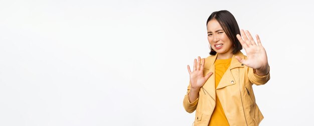 Hören Sie auf, sich von mir zurückzuziehen Konzept Junge angewiderte asiatische Frau, die von etwas geblendet wird, das die Hände in der Verteidigung ausstreckt und das Licht blockiert, das über weißem Hintergrund steht