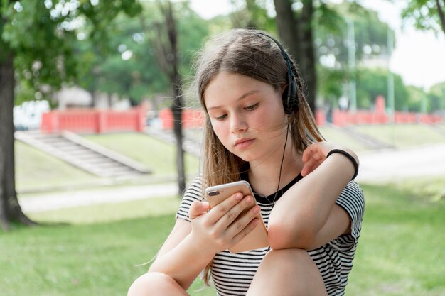 Hörende Musik der schönen Jugendlichen bei der Anwendung des Mobiltelefons am Park